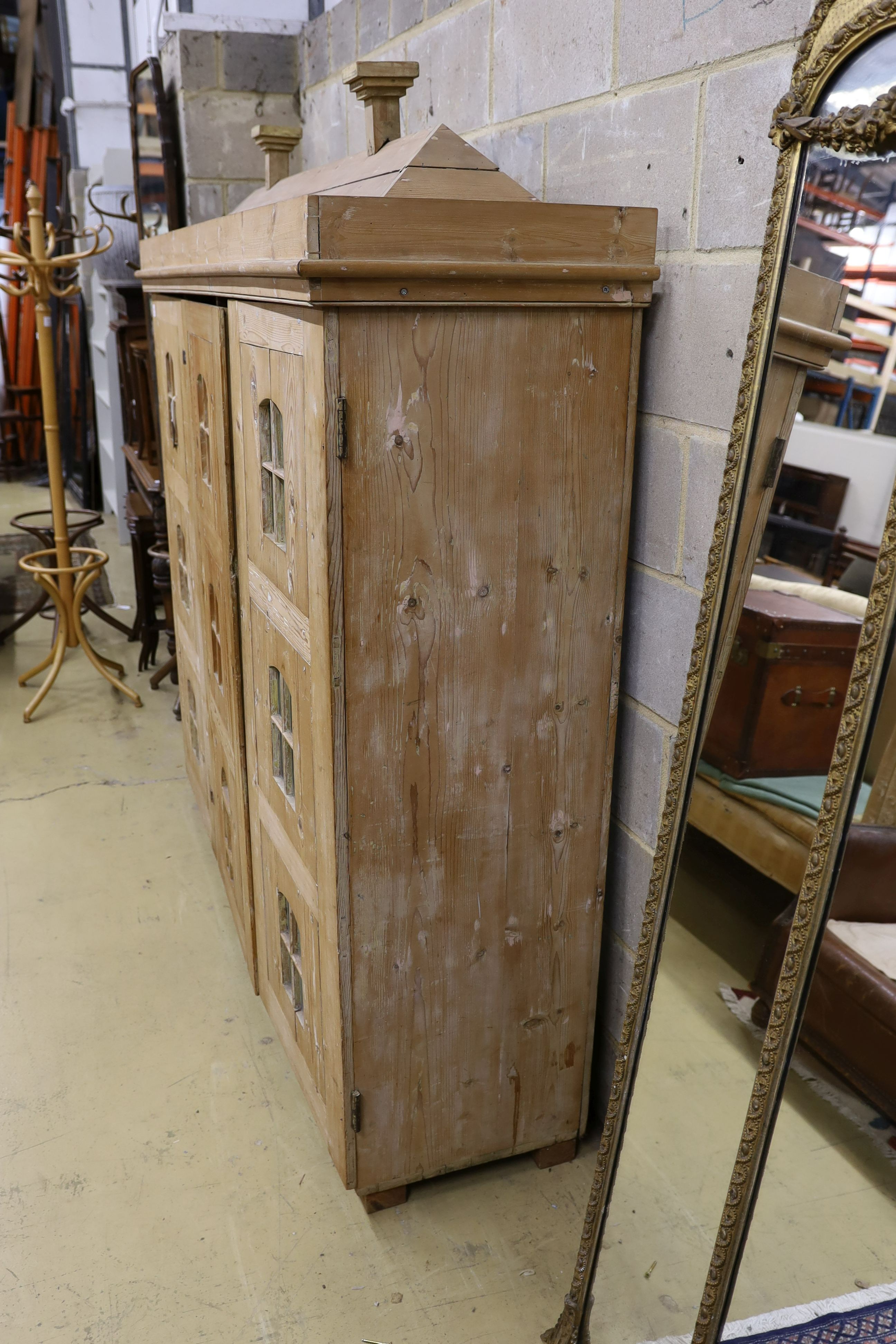 A 19th century stripped pine hall cupboard modelled as a dolls house the two door nine window facade enclosing a compartmented interior, width 182cm, depth 46cm, height 192cm